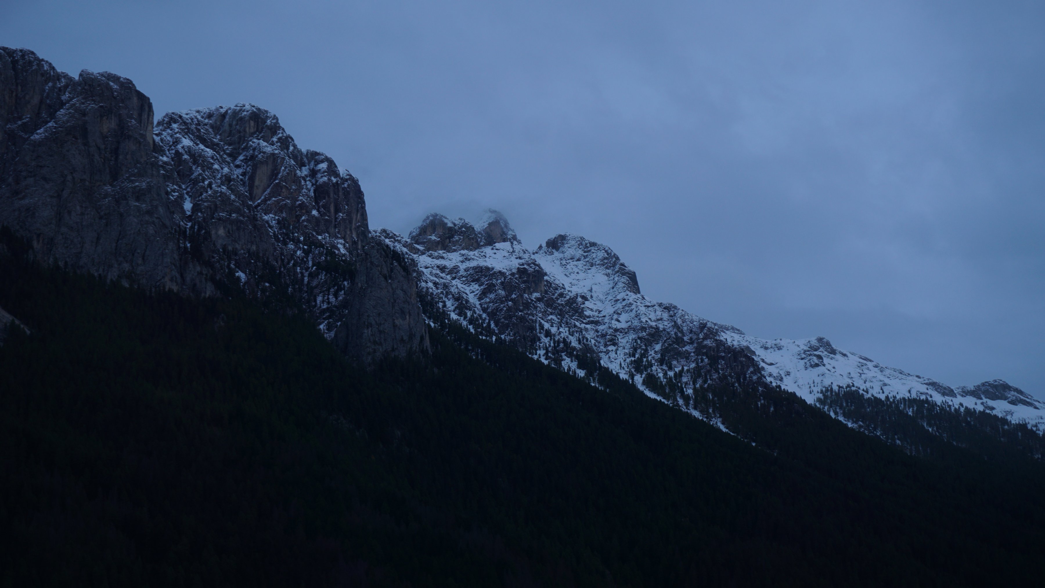 Ein teilweise schneebedeckter Gebirgszug unter dunklem Himmel. Wolken. Abend.